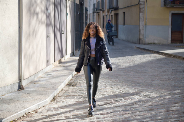 Una afro chica negra feliz con el pelo castaño rizado camina por la calle sonriendo
 - Foto, imagen