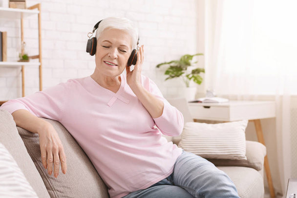 Senior woman listening audiobook in headphones, free space - Foto, imagen