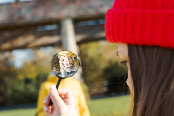 Girl in a red knitted hat looking through a magnifier on a boy - Fotoğraf, Görsel