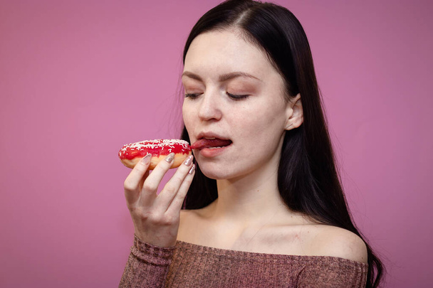 Κοντινό πορτρέτο ενός ικανοποιημένου όμορφου κοριτσιού που τρώει ντόνατς απομονωμένο σε ροζ φόντο - Φωτογραφία, εικόνα