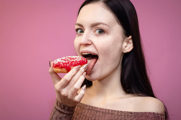 close-up portret van een blij mooi meisje eten donuts geïsoleerd over roze achtergrond - Foto, afbeelding