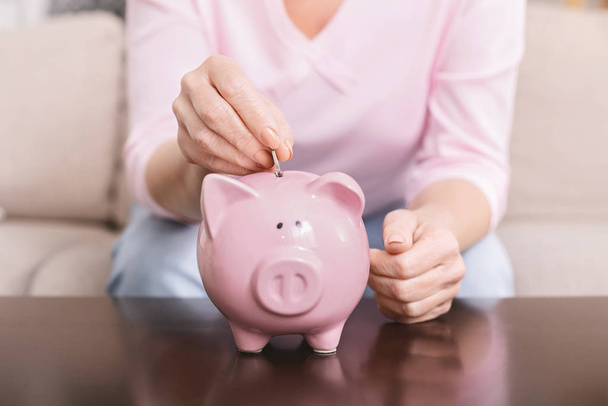 Mature woman putting coin into piggy bank at home - Photo, Image