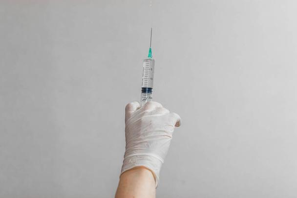 Mão usando luva de látex segurando seringa com um medicamento em fundo branco
 - Foto, Imagem