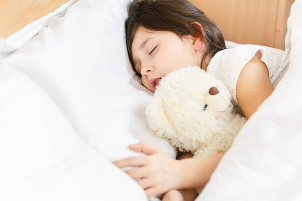 lány alszik egy puha játék fehér ágyban - Fotó, kép