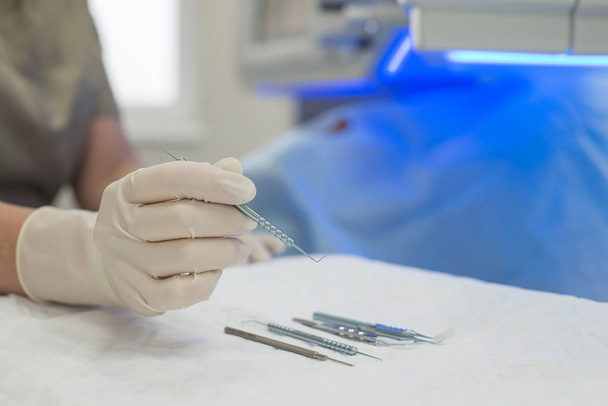 Steril bir masanın üzerinde elinde mikroskobik göz ameliyatı için aletler tutan bir göz doktorunun yakın çekimi. - Fotoğraf, Görsel