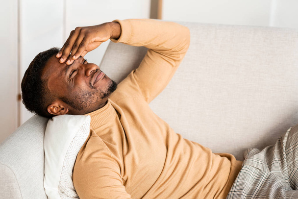 Homme ayant mal à la tête souffrant de douleur allongée sur le canapé intérieur
 - Photo, image