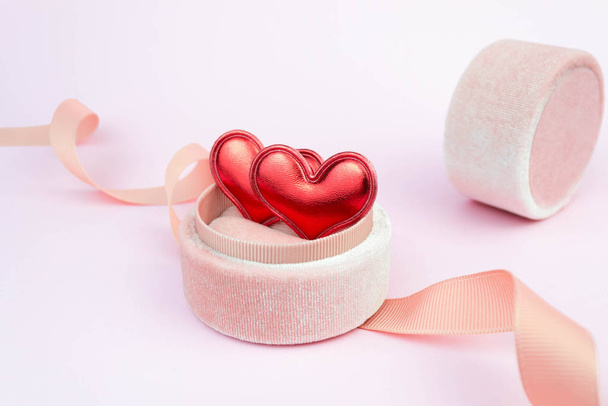 Two red hearts in a ring box with ribbon on soft pink background. Romantic symbol gift. Couple date concept - Fotografie, Obrázek