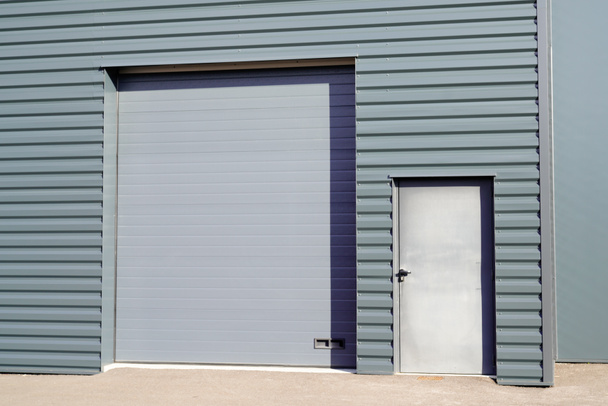 graue Metall-Rollläden an vertikal profilierten Platten graues neues Industriegebäude - Foto, Bild