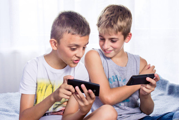 Boys, brothers playing online games on their smart phones. Modern child activity - Φωτογραφία, εικόνα