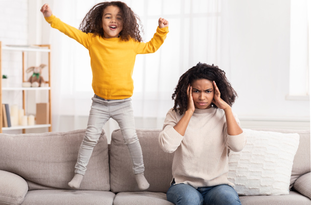 Tired Mother Covering Ears, Daughter Jumping On Couch At Home - Photo, Image