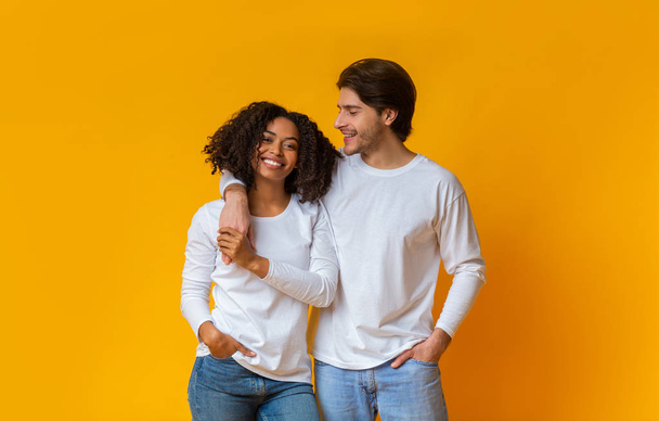 gelukkig multiraciaal paar knuffelen en poseren samen over gele achtergrond - Foto, afbeelding