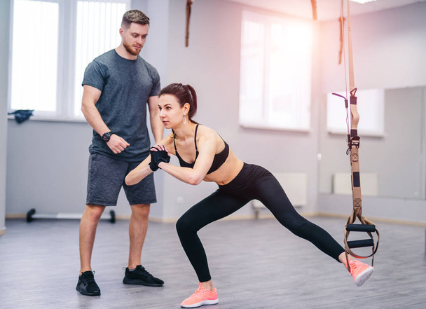 Personal trainer working with his client in gym. Young and beautiful woman working out with dumbbells in gym. Healthy life and sport fit. Fitness concept - Photo, image