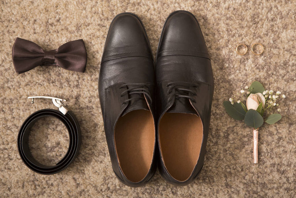 Αξεσουάρ γαμπρού και μαύρα παπούτσια σε καφέ φόντο δαπέδου - Φωτογραφία, εικόνα