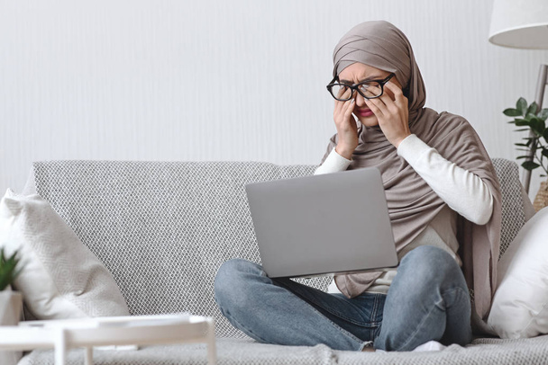 Arabische vrouw met gezichtsvermogen probleem na het werken op laptop thuis - Foto, afbeelding