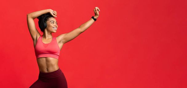 fröhliches sportliches Mädchen mit Headset, das über rotem Hintergrund tanzt - Foto, Bild