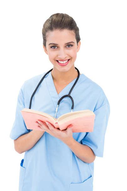 Happy nurse in blue scrubs holding a book - Foto, afbeelding