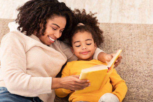 Mother And Daughter Reading Book Sitting On Sofa At Home - Photo, Image