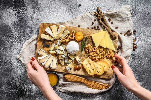 Şefin elleri fındık ve incirle servis edilen peynir tabağını tutuyor. Gri arka plan. Üst görünüm - Fotoğraf, Görsel
