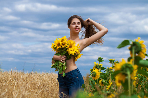 Sexy girl with a bouquet of sunflowers posing on a field backgro - Фото, зображення