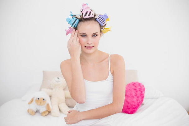 Calm woman in hair curlers touching her face - Фото, изображение