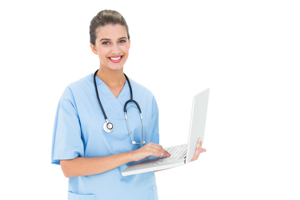 Cheerful nurse in blue scrubs using a laptop - Valokuva, kuva
