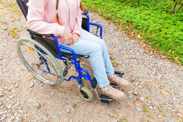 Pernas pés handicap mulher na roda de cadeira de rodas na estrada no parque hospitalar à espera de serviços de pacientes. Menina paralisada irreconhecível em cadeira inválida para pessoas com deficiência ao ar livre. Conceito de reabilitação
. - Foto, Imagem