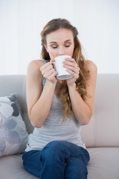 Young woman sitting on sofa drinking from mug - Foto, imagen