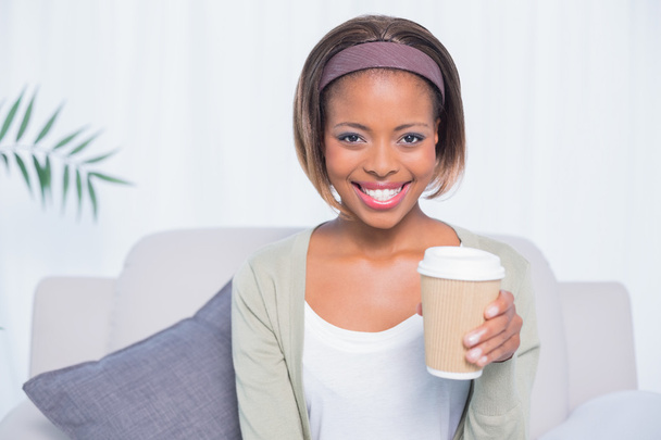Smiling woman sitting on sofa holding coffee - Фото, изображение