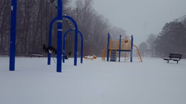 Speelpark voor kinderen tijdens de sneeuwval in de winter. Speeltuin tijdens het sneeuwen met sneeuw op de grond tijdens de dag. - Video