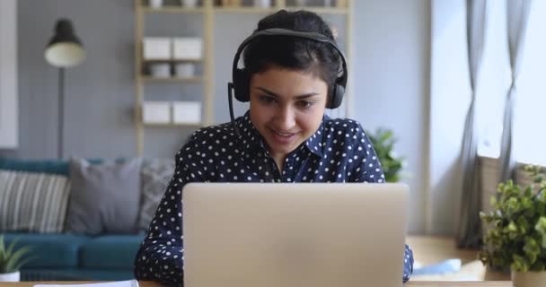 Smiling indian woman wear wireless headset video calling on laptop - 映像、動画