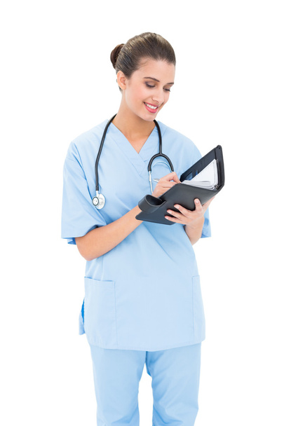 Attractive nurse in blue scrubs filling an agenda - Foto, afbeelding