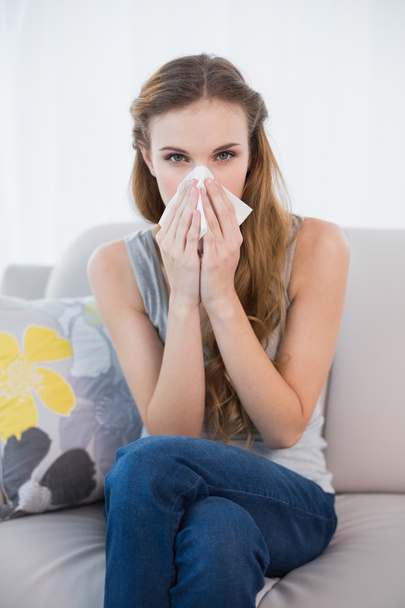 Sick woman sitting on sofa blowing her nose - Фото, зображення