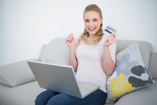 Casual thrilled blonde holding credit card and laptop - Φωτογραφία, εικόνα