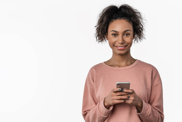 Retrato da jovem africana sorridente de pé e usando telefone celular sobre fundo branco
 - Foto, Imagem
