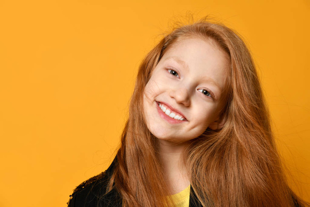 rothaarige Teenager in schwarzer Jacke. sie lächelt und schaut dich an, posiert vor orangefarbenem Studiohintergrund. Nahaufnahme - Foto, Bild
