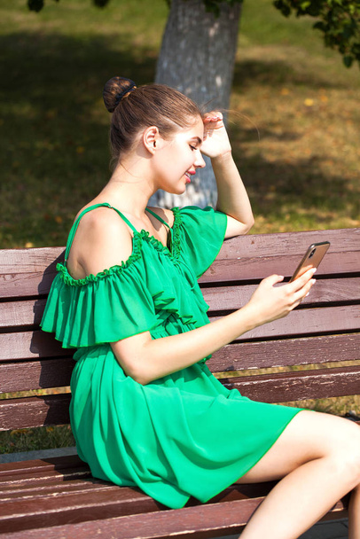 Sexy beautiful caucasian girl in green dress sitting on a bench  - 写真・画像
