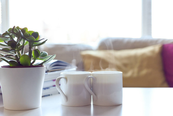 現代的な家庭でコーヒーテーブルとホットドリンク付きのリラックスしたソファエリア - 写真・画像