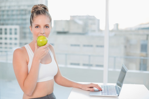 Sporty blonde eating apple while using laptop - Foto, Imagem