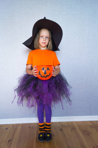 A little girl in a witch suit holds a pumpkin - Foto, imagen
