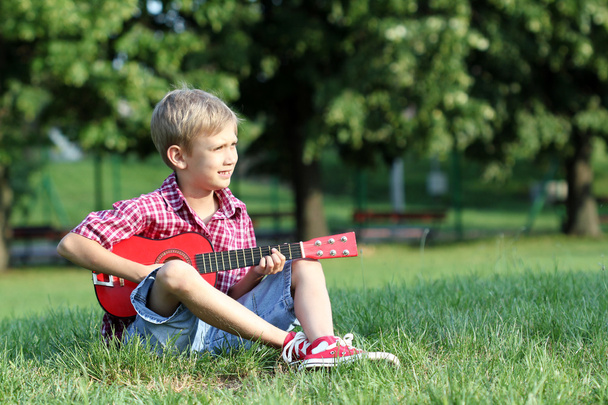мальчик сидит на траве и играет на гитаре
 - Фото, изображение