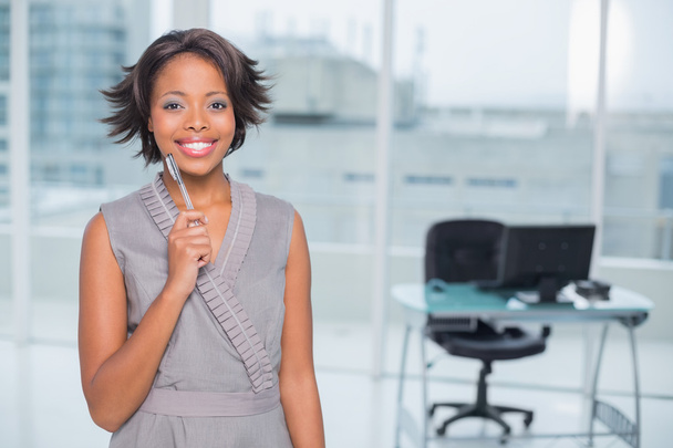 Smiling businesswoman standing in her office holding pen - Foto, afbeelding