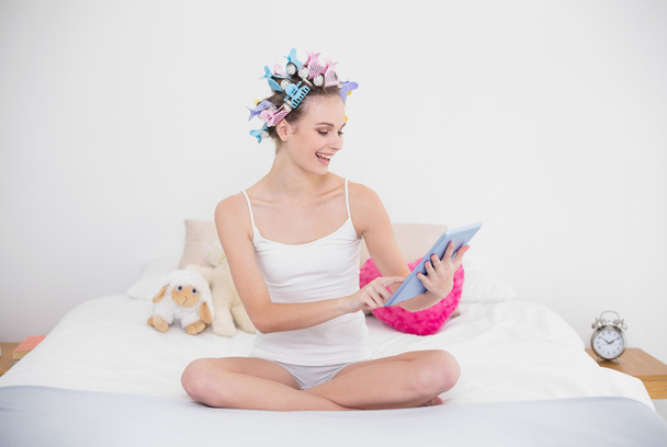 Delighted woman in hair curlers using a tablet pc - Foto, afbeelding