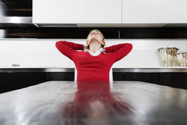 woman in red dress sitting in the kitchen - Фото, зображення