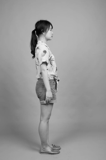 Studio shot of young beautiful Asian tourist woman ready for vacation against gray background in black and white - Фото, изображение