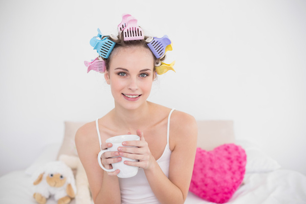 Pleased woman in hair curlers holding a cup of coffee - Fotó, kép