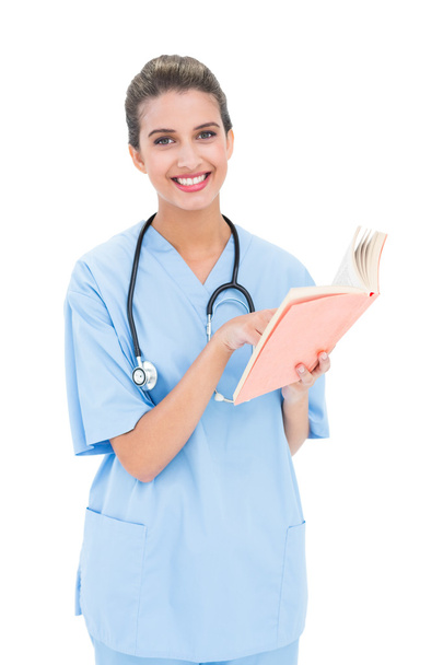 Pleased nurse in blue scrubs holding a book - Zdjęcie, obraz
