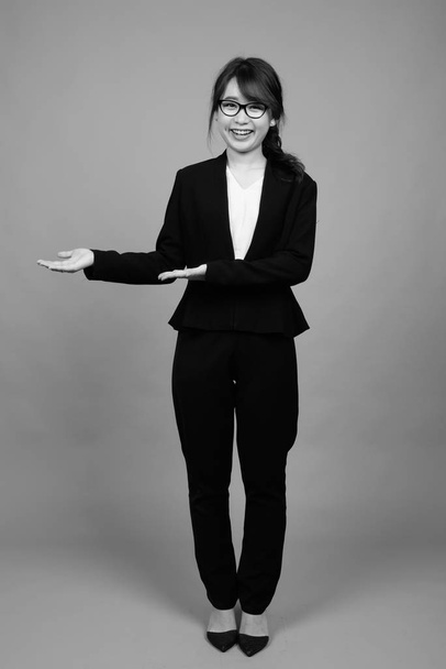 Studio shot of young beautiful Asian businesswoman wearing eyeglasses against gray background in black and white - Fotoğraf, Görsel