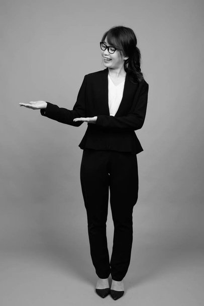 Estudio de tiro de joven hermosa mujer de negocios asiática con gafas graduadas sobre fondo gris en blanco y negro - Foto, imagen