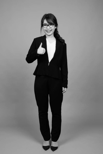 Studio shot of young beautiful Asian businesswoman wearing eyeglasses against gray background in black and white - 写真・画像