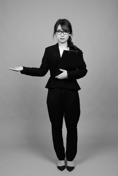 Studio laukaus nuori kaunis aasialainen liikenainen yllään silmälasit harmaata taustaa vasten mustavalkoinen - Valokuva, kuva